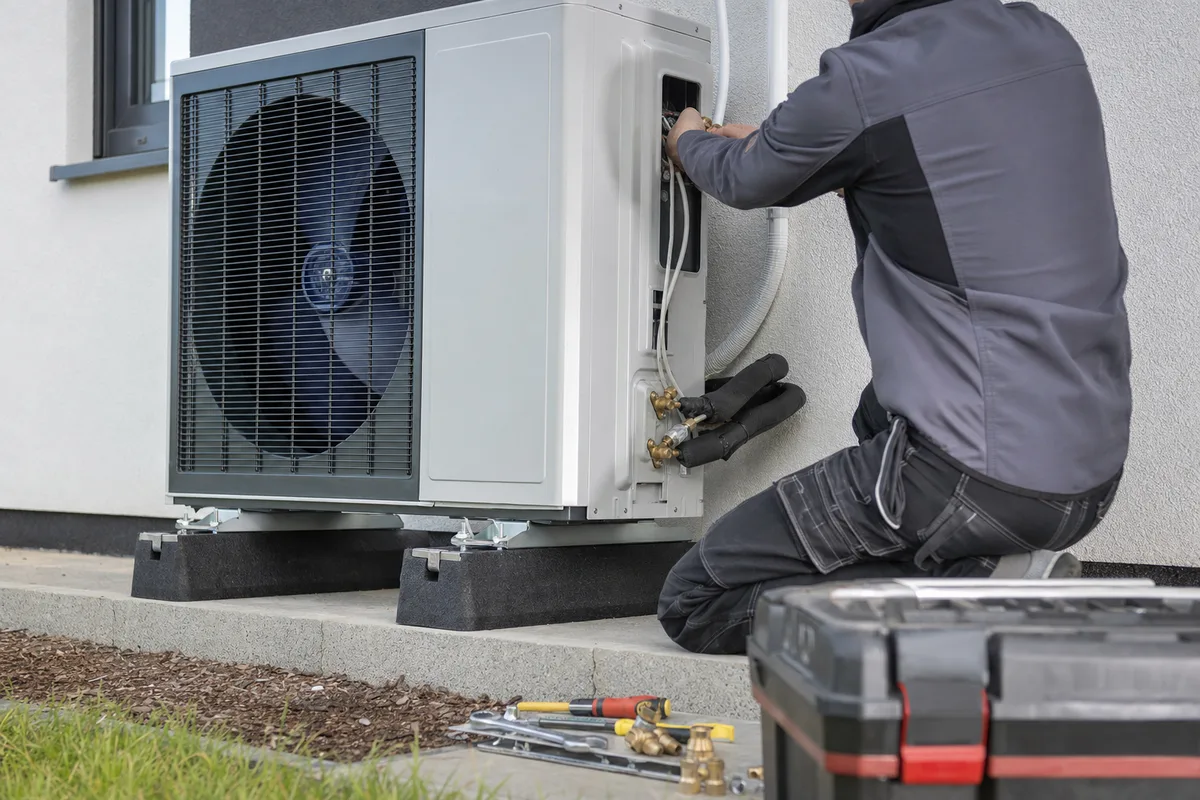 Technicien installant l’unité extérieure d’une pompe à chaleur devant une maison